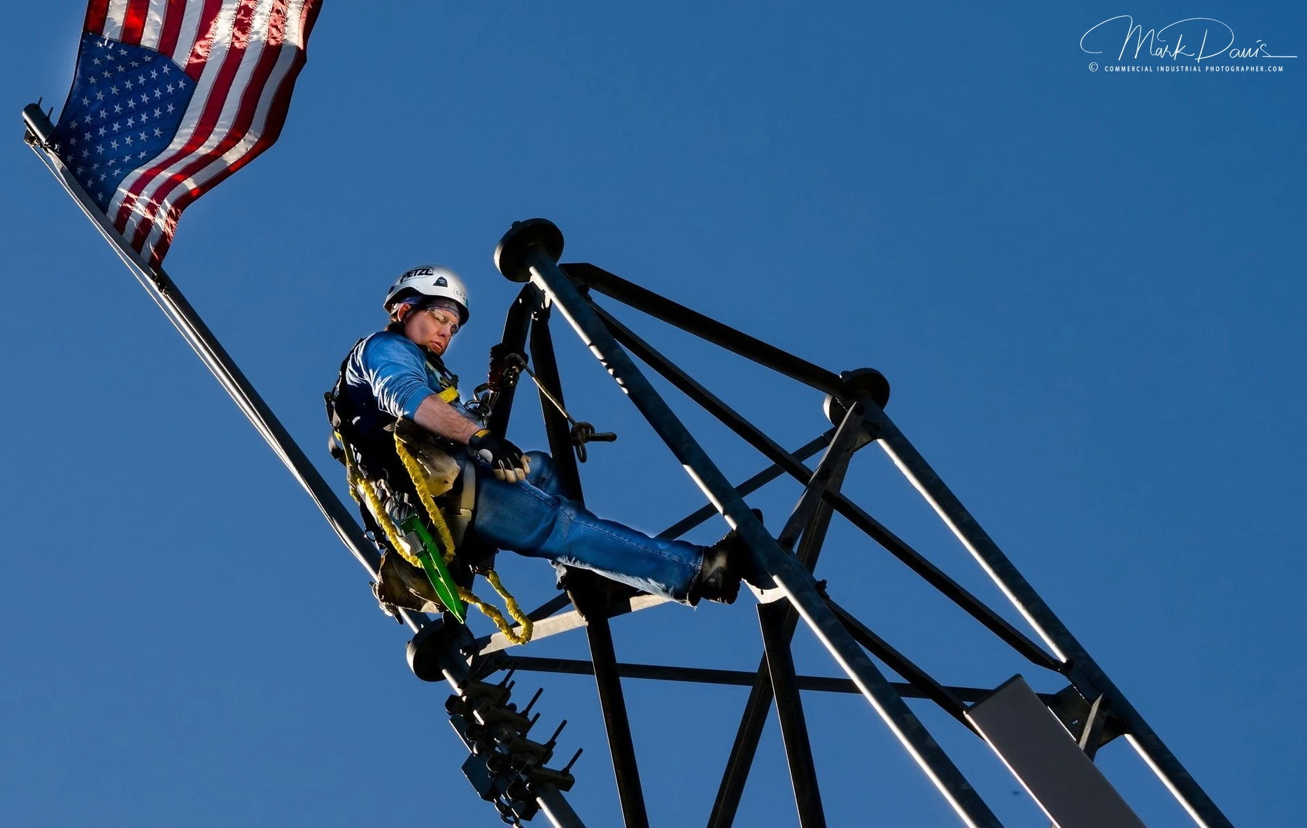 Tower rigger climbing steel structure with an American flag overhead